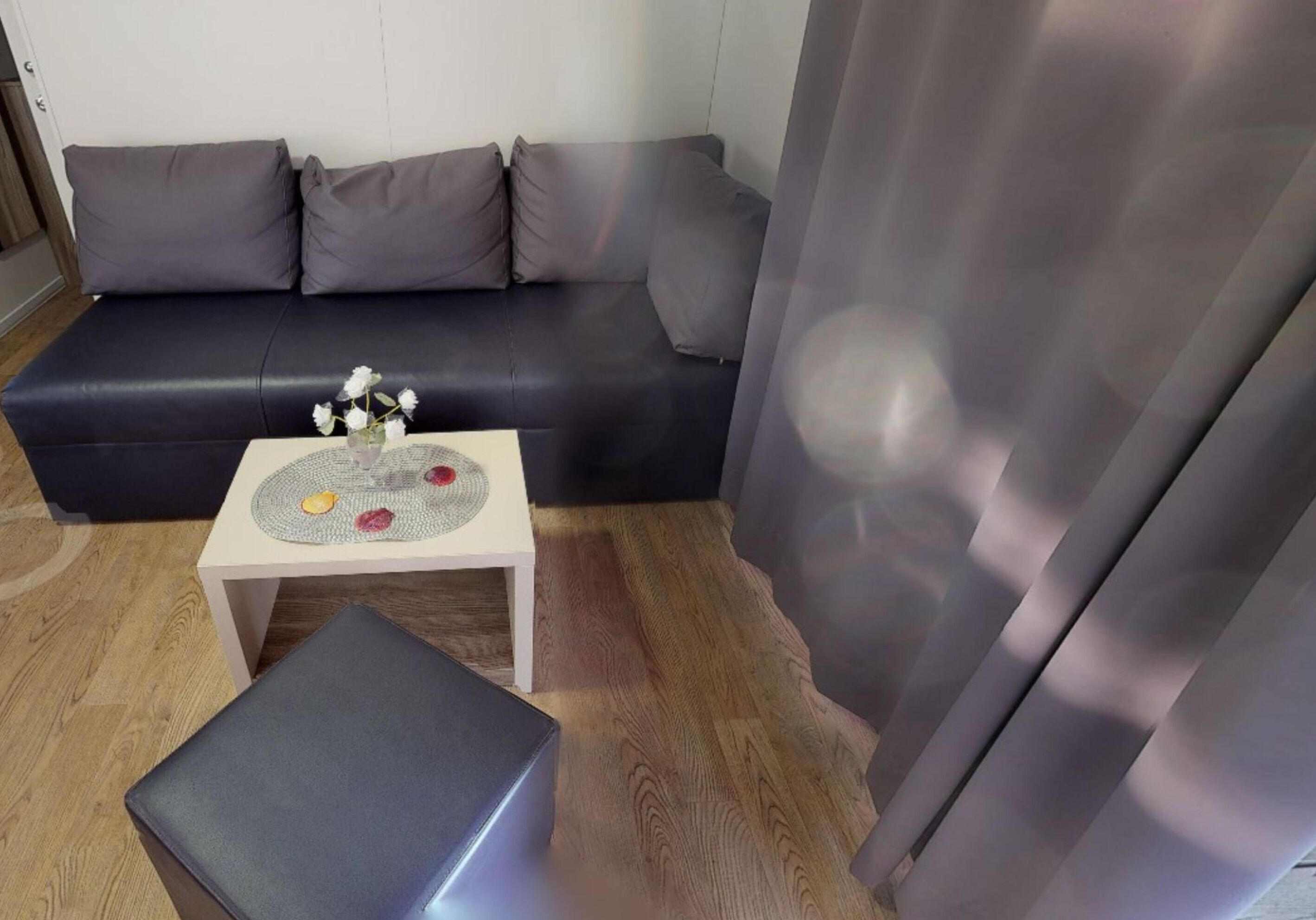A modern living room with a dark grey sofa, a small white side table with a decorative tray, and a grey ottoman.
