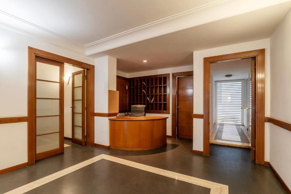A hallway with a reception desk, wooden doors, and a tiled floor.