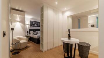 A modern hotel room with a round white table, a black trash bin, a white sofa, and a large mirror.