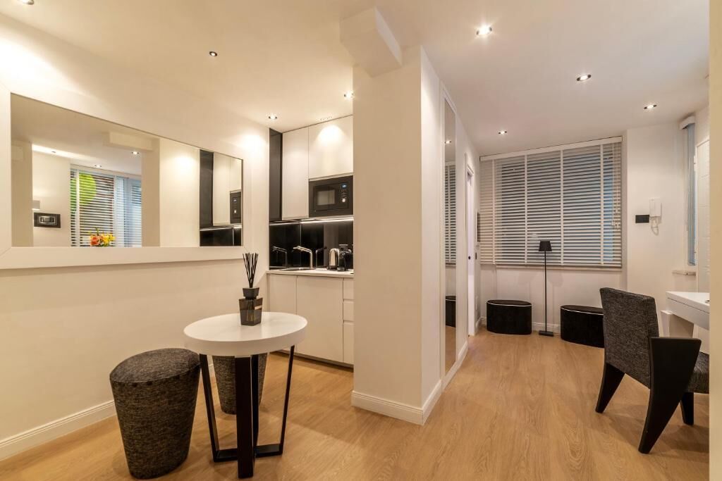 A modern kitchen with white cabinets, a microwave, and a sink. There is a dining area with a round table and two chairs.