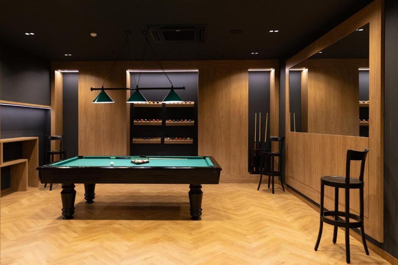 A billiards room with a pool table, green hanging lamps, and shelves with billiard balls.