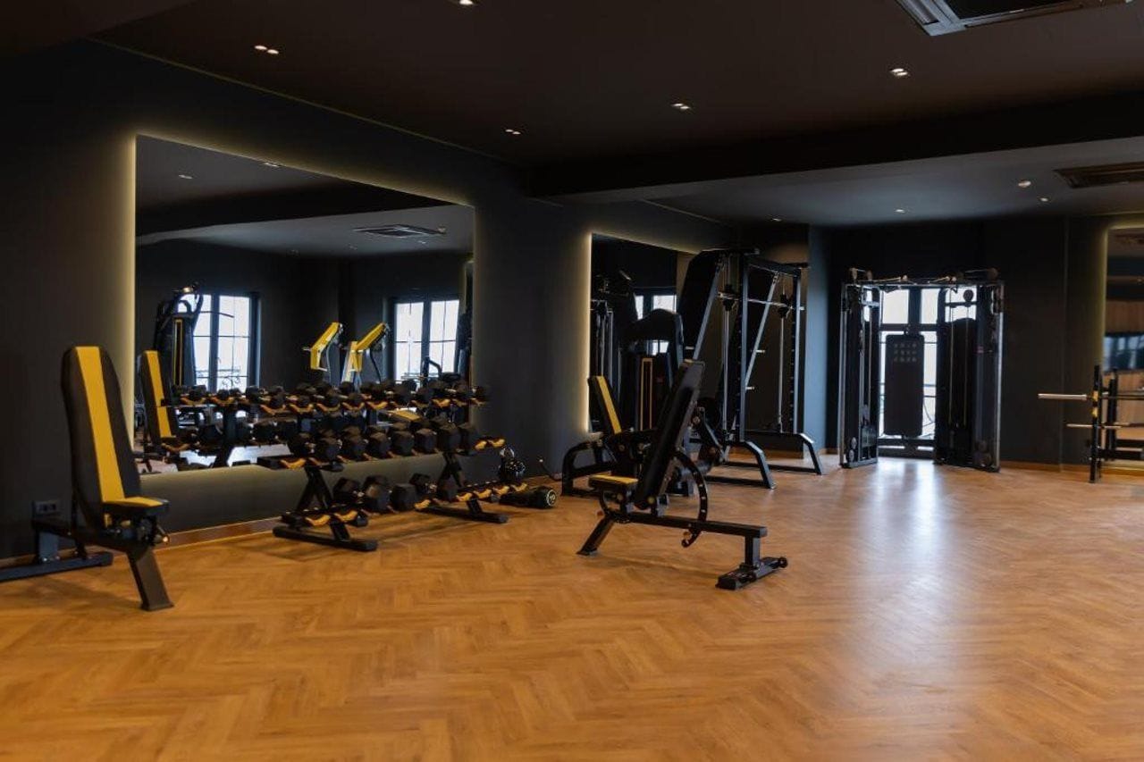 A gym with various exercise equipment, including dumbbells and weight machines, and a wooden floor.