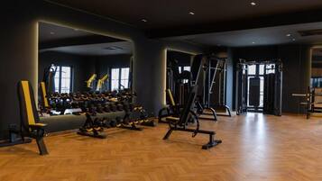 A gym with various exercise equipment, including dumbbells and weight machines, and a wooden floor.