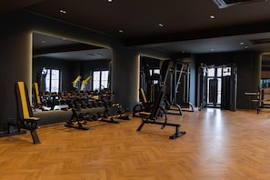 Un gimnasio con diversos equipos de ejercicio, incluyendo mancuernas y máquinas de pesas, y suelo de madera.