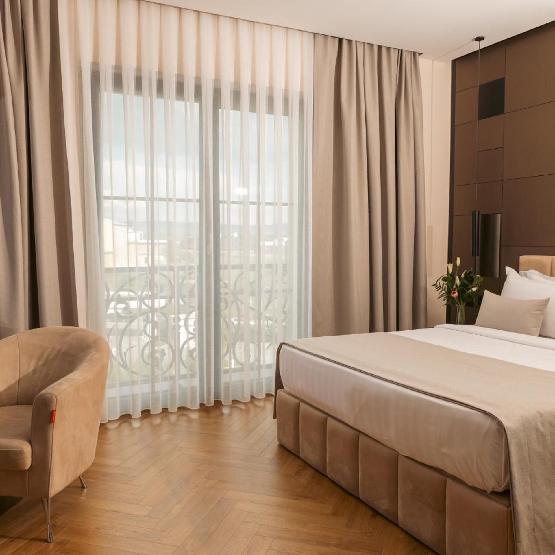 Una habitación de hotel con cama, una silla y un balcón con cortinas.