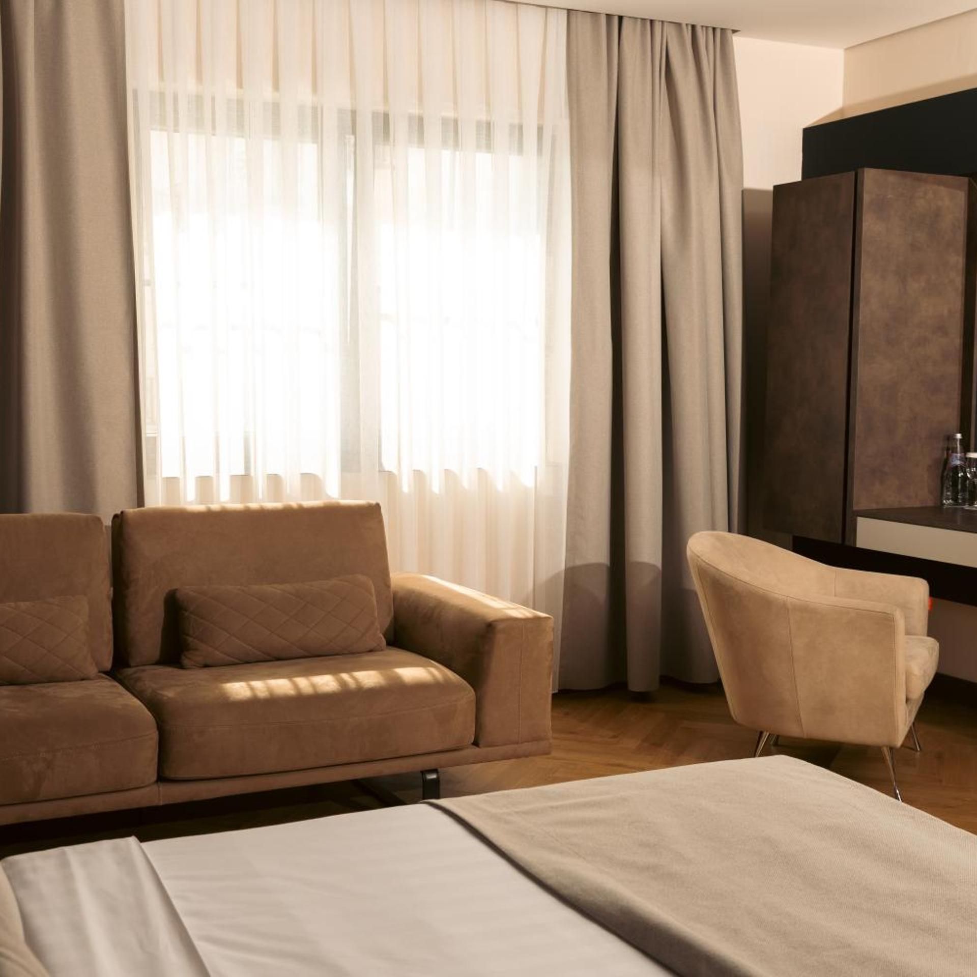 Una habitación de hotel con cama, sofá, sillón y escritorio con archivador.