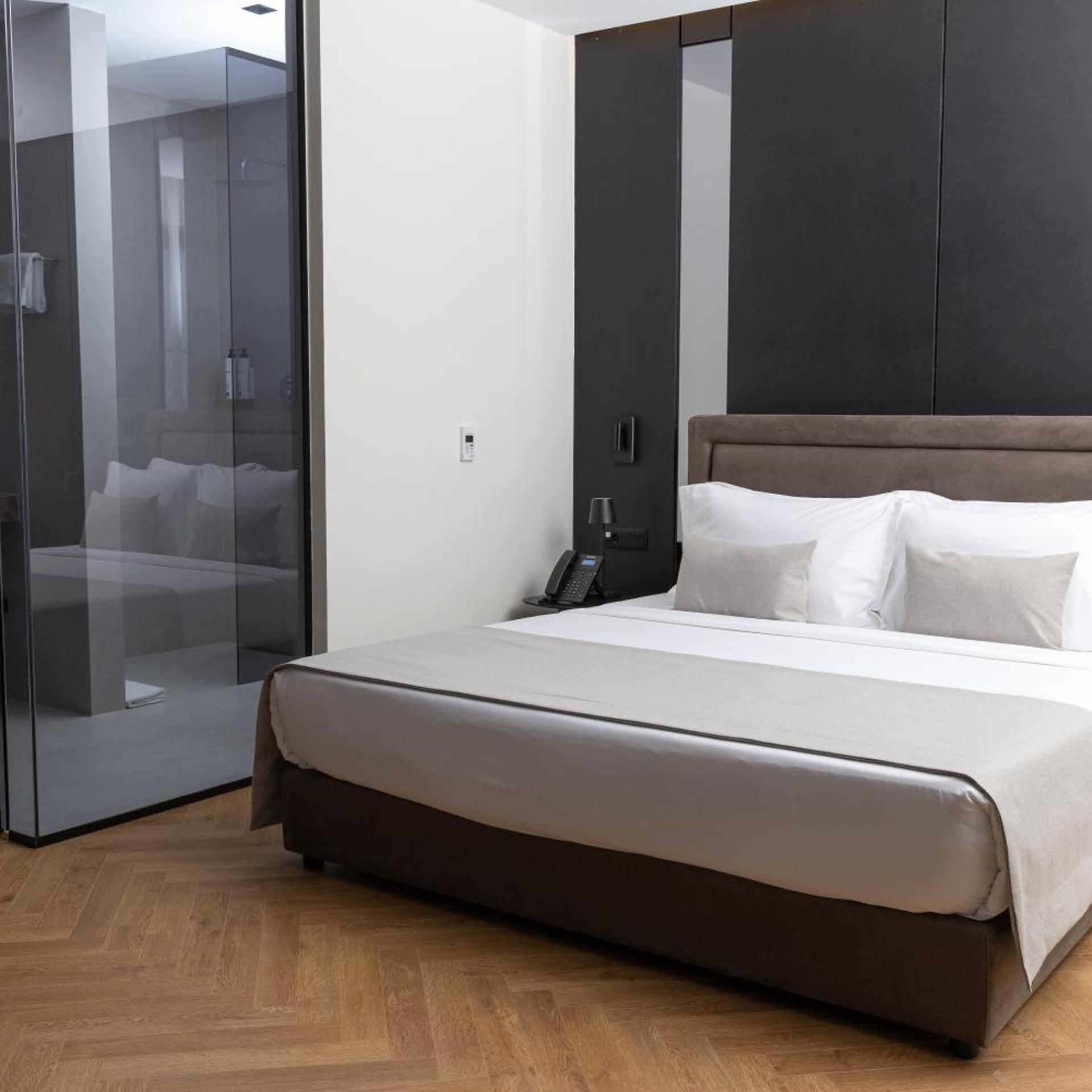 Habitación de hotel moderna con una cama grande, cabina de ducha de vidrio y un armario oscuro.