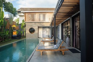A modern pool area with lounge chairs, a concrete pool, and a wooden deck. - VILLA NANDI (Kerobokan)