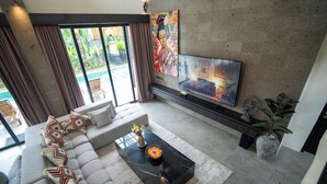 A modern living room with a large flat-screen TV, a sectional sofa, and a coffee table with decorative pillows. - VILLA NANDI (Kerobokan)