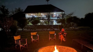 Un foyer avec des chaises disposées autour, une structure couverte en arrière-plan et une personne assise sur une chaise.