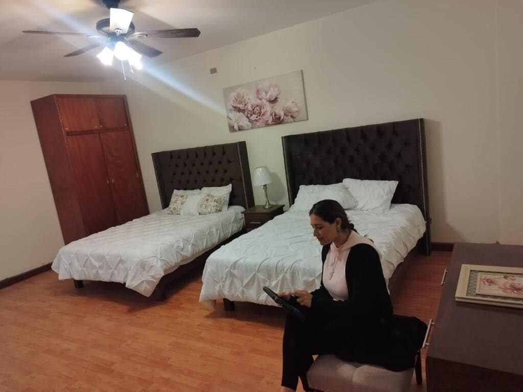 A hotel room with two beds, a ceiling fan, a wooden wardrobe, and a painting on the wall.