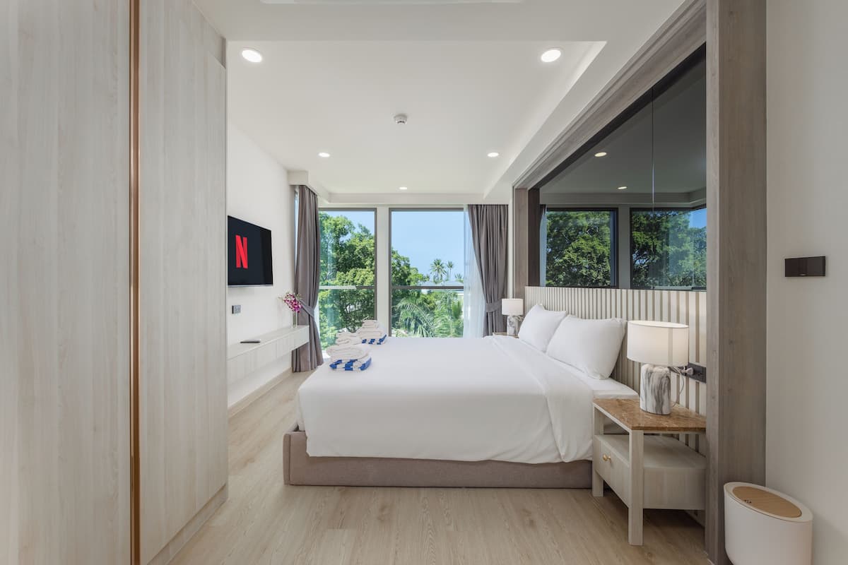 A modern hotel room with a large bed, a TV mounted on the wall, and a view of the outdoors.