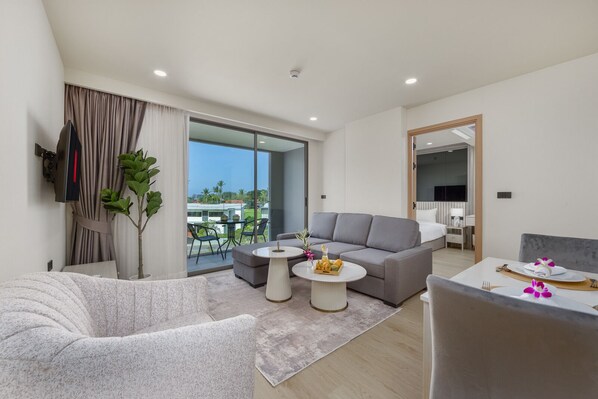 Una habitación de hotel moderna con un sofá gris, una mesa redonda de centro y una mesa de comedor con platos y flores.