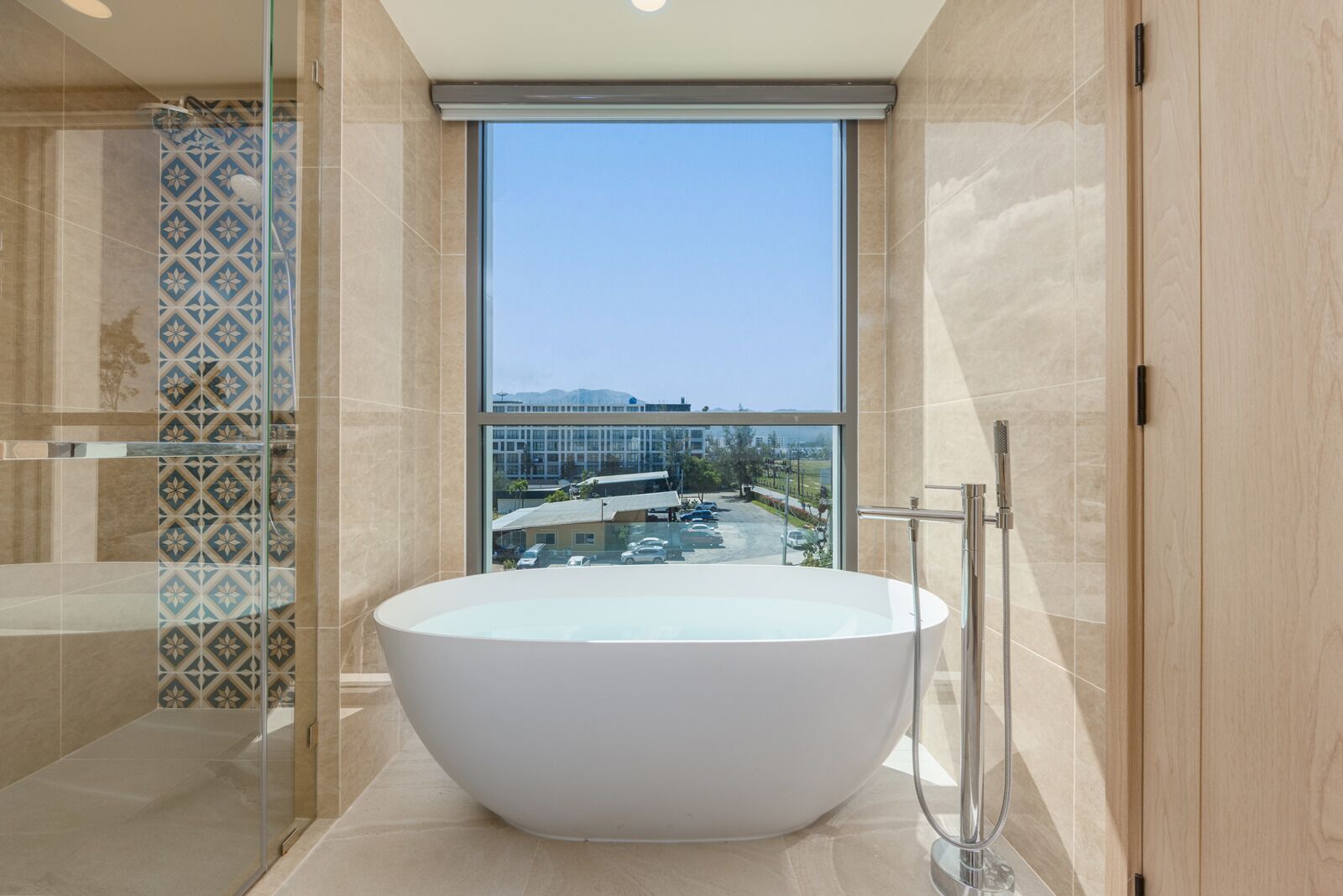 A modern bathroom with a large bathtub, a shower area, and a view of a parking lot and buildings through a large window.