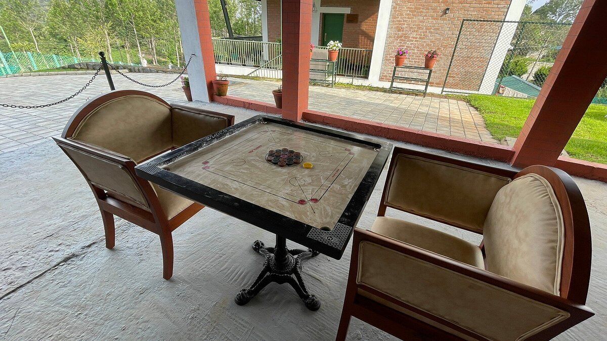 A covered patio area with a table and two chairs, a chain barrier, and a view of a brick building and greenery.