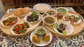 Una mesa con diversos platos, incluyendo samosas, pan plano y varios recipientes con salsas.