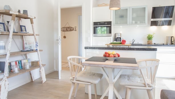 Een moderne keuken met witte kasten, een centraal eiland met een fruitschaal, en een houten ladderplank met boeken.