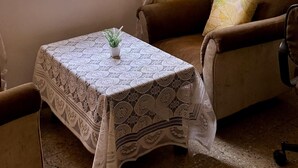 Una habitación acogedora con ventana, una mesa con mantel de encaje, un sofá marrón y luces de cuerda.