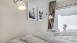 A modern hotel room with a large bed, two wall-mounted lamps, and two framed pictures on the wall.