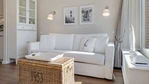 A white sofa with cushions, a wicker basket, a cabinet with glass doors, and two wall-mounted lamps.