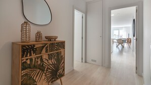 Ein modernes Interieur mit einem Holzkabinett mit tropischen Blattmotiven, einem großen ovalen Spiegel und einem Essbereich im Hintergrund.