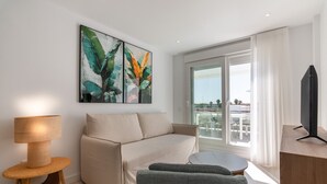 Ein modernes Wohnzimmer mit einer Couch, einem kleinen runden Tisch, einer Lampe und einem Fernseher auf einem Holzgestell.