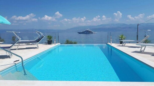 A pool with lounge chairs and a view of the sea and mountains.