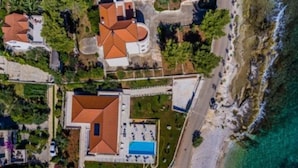 An aerial view of a coastal property with multiple buildings, a swimming pool, and a beach.