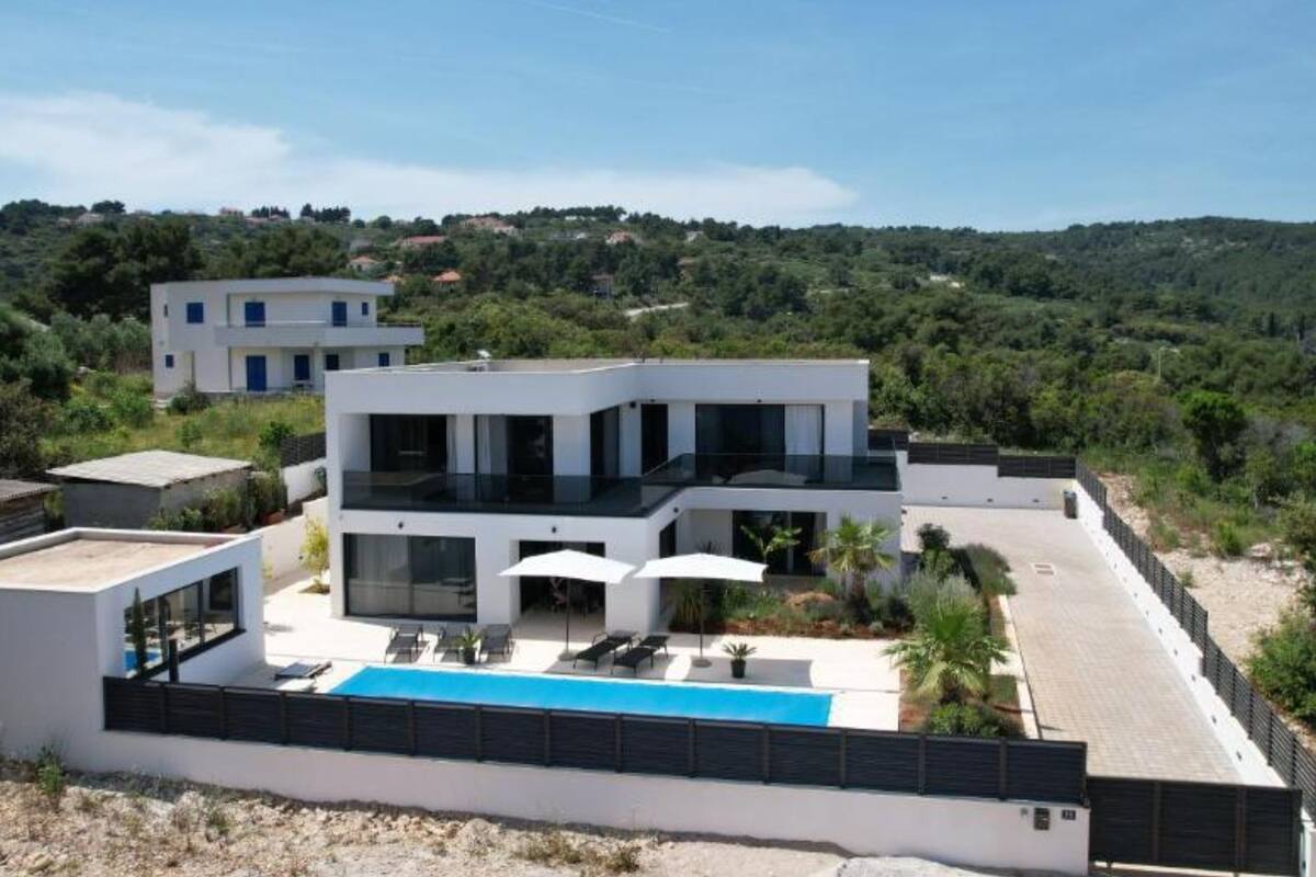A modern two-story house with a rooftop pool, surrounded by greenery and hills.