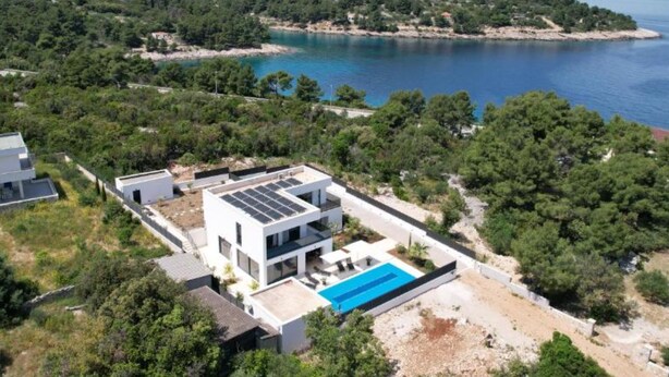 Una villa moderna con piscina, rodeada de exuberante vegetación y vistas al mar.