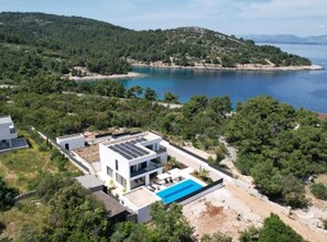 A modern villa with a swimming pool, surrounded by lush greenery and a view of the sea. - Sunset Villa Aves With Pool, Gym and Sauna (Rogac)