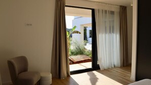 Un dormitorio moderno con un amplio ventanal corredera que da a un patio. Hay una silla y un pequeño reposapiés en la habitación.
