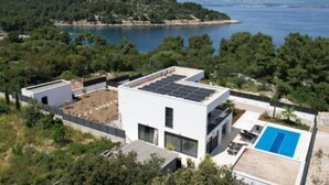 Una casa moderna con un sistema de paneles solares en la azotea, una piscina y vistas a un lago y colinas.
