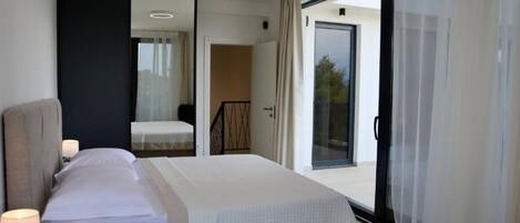 Quarto moderno com cama grande, mesa de cabeceira com abajur, espelho e porta de vidro deslizante para uma varanda.