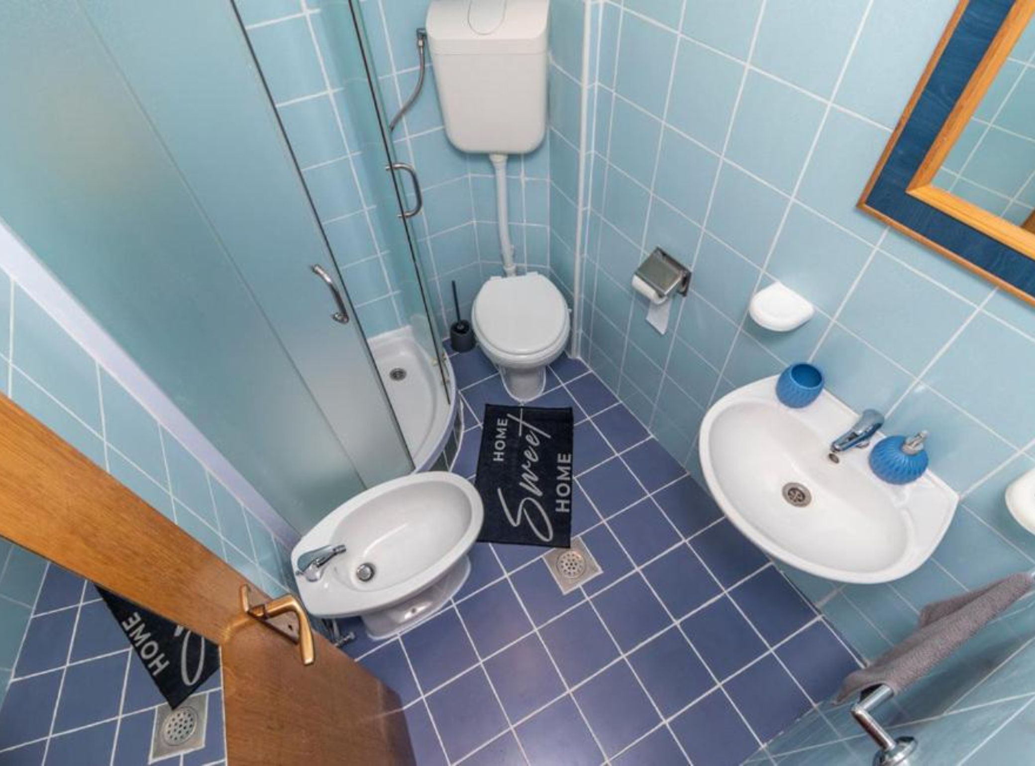 Une salle de bain comprenant des toilettes, un bidet et un lavabo, dont le carrelage présente un motif bleu clair.