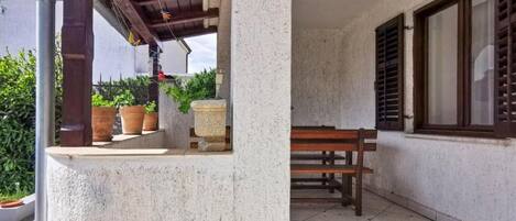 A covered outdoor area with a bench, potted plants, and a stone structure.