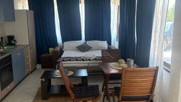 A compact room with a bed, a small kitchenette, a dining area with a table and chairs, and a window with curtains.