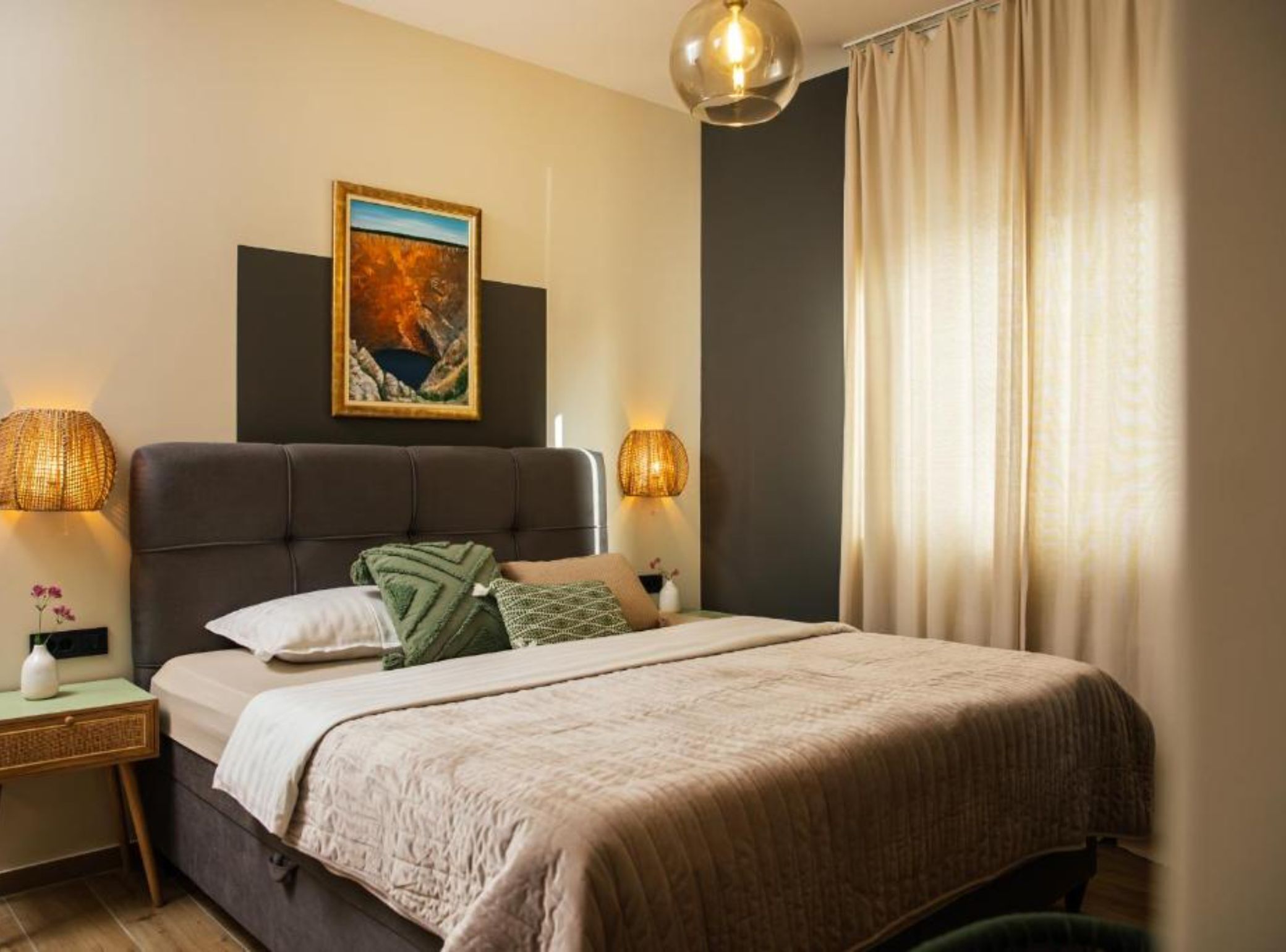 Een slaapkamer met een bed, twee bedlampen, een schilderij en een raam met gordijnen.