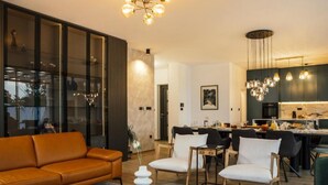 A modern living room with a leather sofa, a glass coffee table, and a dining area with chairs and a kitchen in the background. - Luxury Villa Lara with Heated Pool, Hot-Tub and Sauna (Zmijavci)