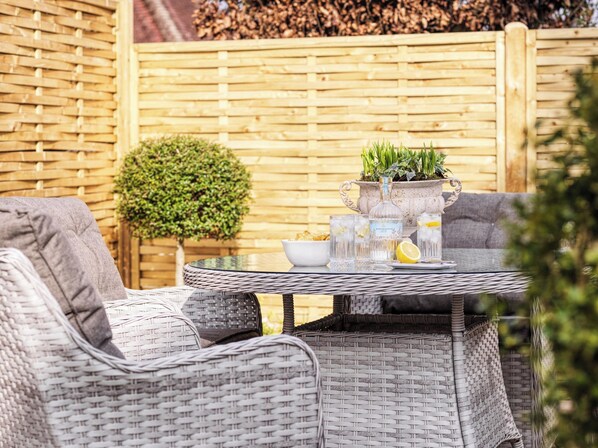 A wicker outdoor seating area with a round table, a potted plant, and a glass of water.