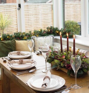 Une table à manger élégamment dressée, avec des assiettes, des verres et des bougies, entourée de décorations festives et de verdure de saison.