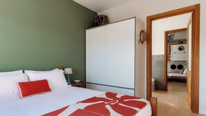 Un dormitorio con cama, armario, mesita de noche y baño a la vista a través de una puerta abierta.