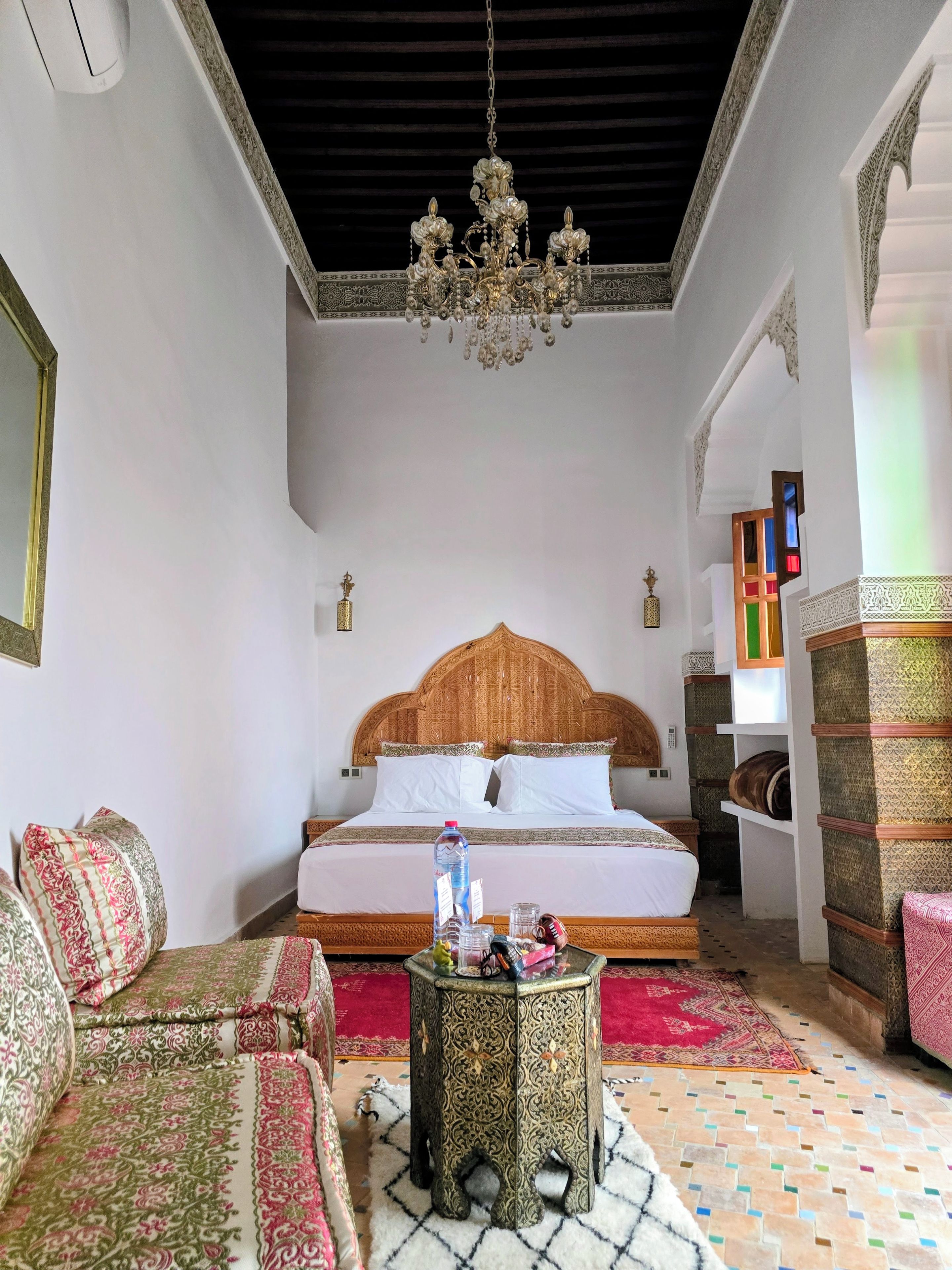 A room with a bed, a sofa, a chandelier, and a patterned rug.
