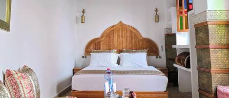 A room with a bed, a sofa, a chandelier, and a patterned rug.