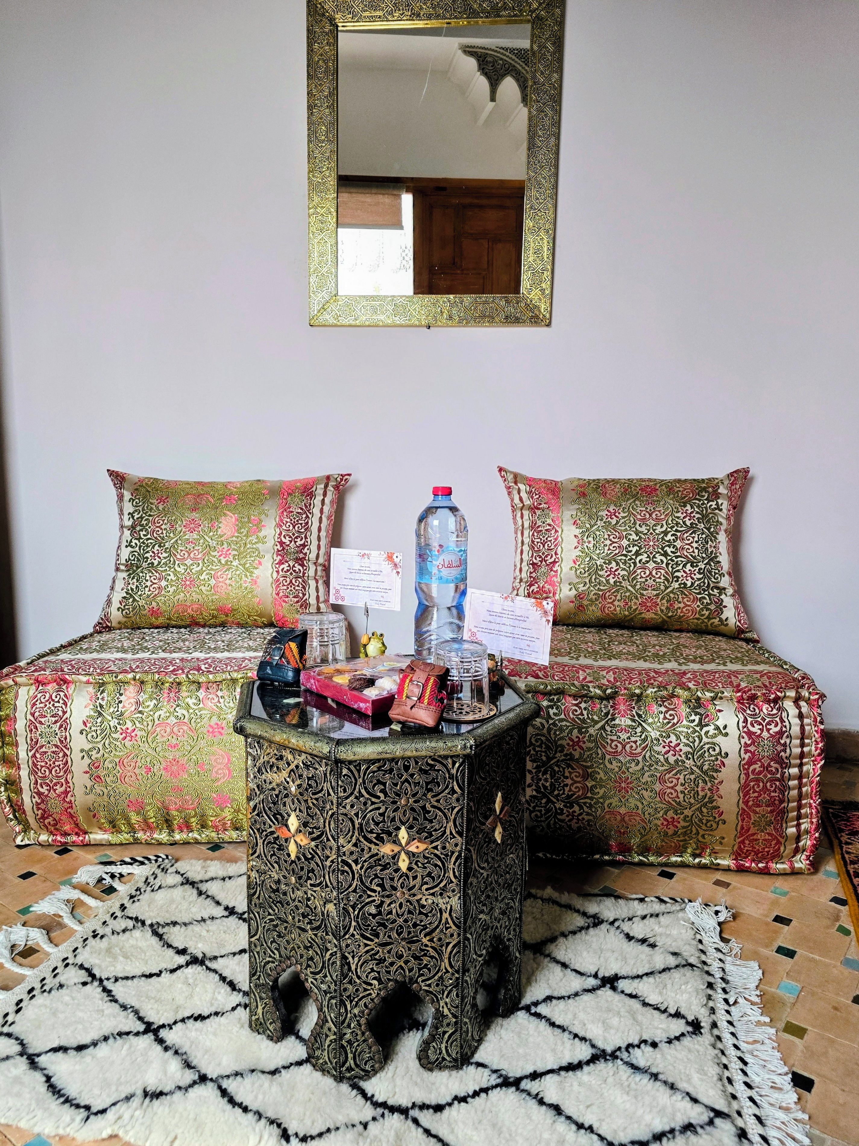 A room with a sofa, a small table with decorative items, a mirror, and a patterned rug.