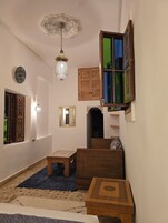 Una habitación con un tapete estampado, un aparador de madera, una mesita pequeña y una lámpara decorativa en el techo.