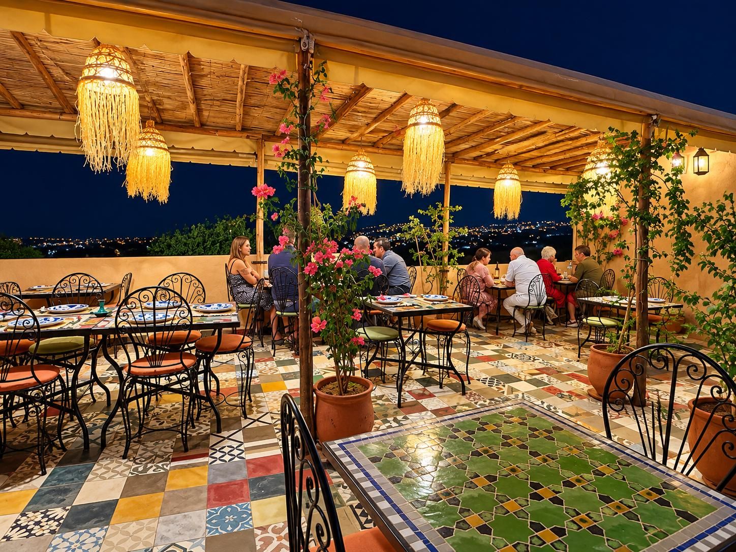 An outdoor dining area with tables and chairs, overhead lighting, and a view of the cityscape at night.