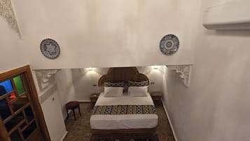 A bedroom with a bed, patterned pillows, a hanging chandelier, and a decorative rug.
