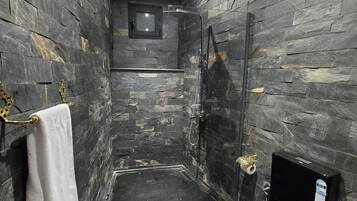 Et moderne badeværelse med stenvæg, glasvæg omkring bruseniche og et sort toilet.