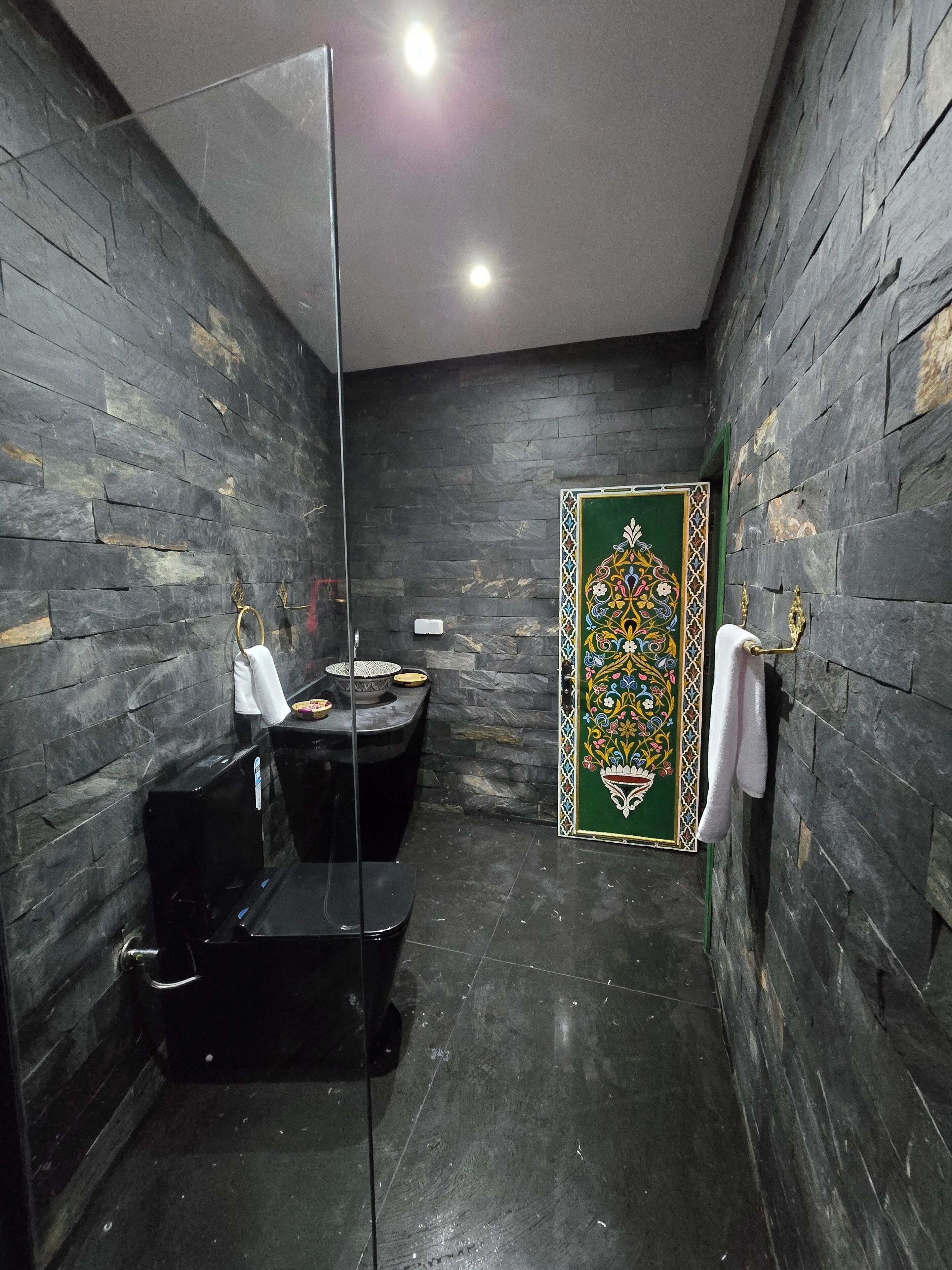 Ein Badezimmer mit dunklen Steinwänden, einer Duschkabine aus Glas, einer Toilette und einer Zierleiste.